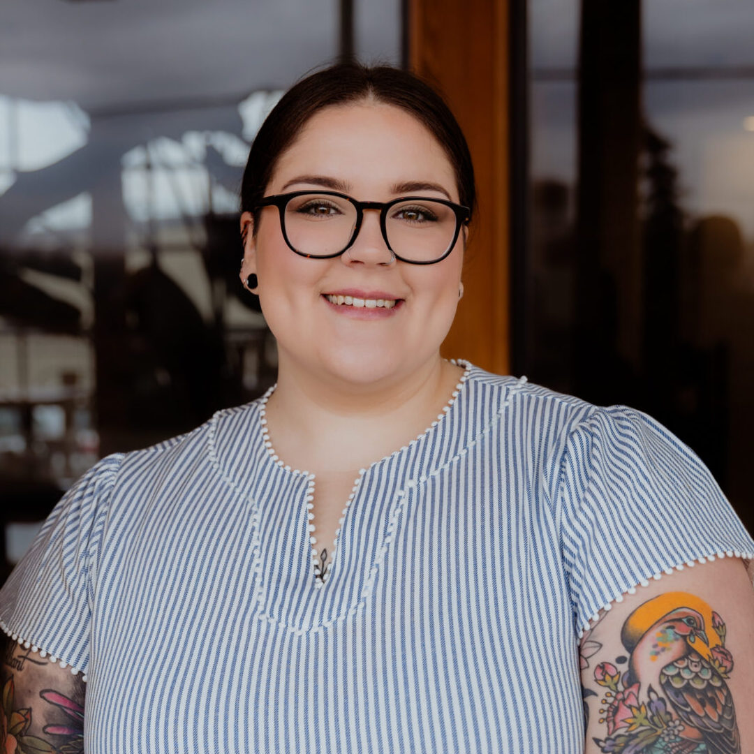 Headshot of Savannah in a striped blue and white shirt, dark hair pinned up, and dark glasses.